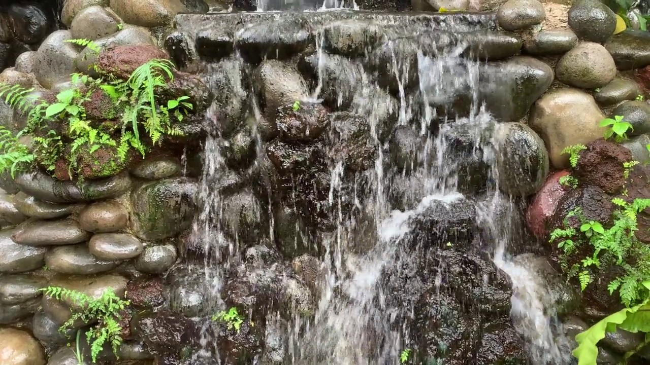 花园里装饰性的小瀑布。清水从石头上流过。景观设计。视频下载