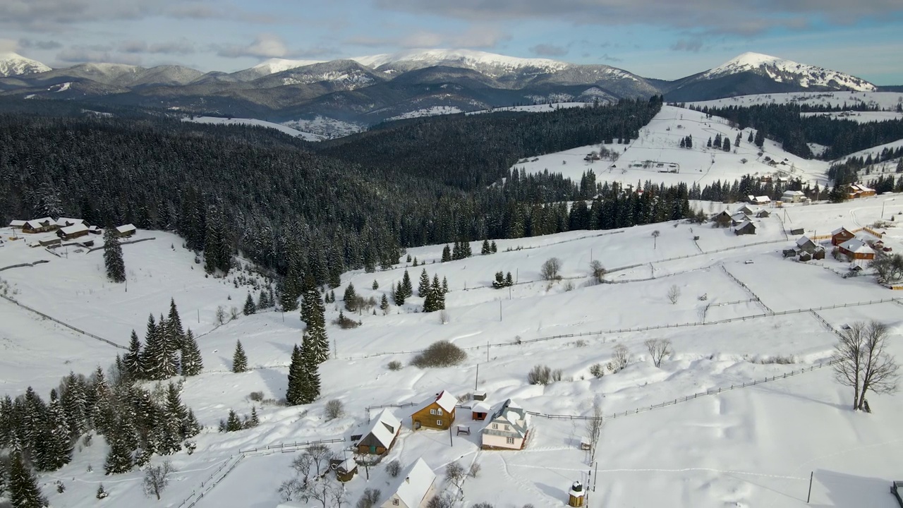 在寒冷的山区，白雪覆盖的森林之间有小村庄的冬季景观视频素材