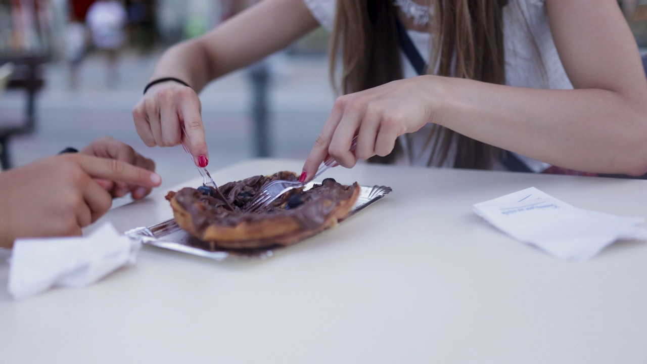 Closeup of teenagers eating a waffle dessert in a sidewalk café.视频素材