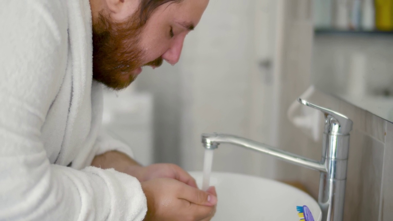 男人在水槽里用水龙头流出的冷水洗脸。实时视频素材