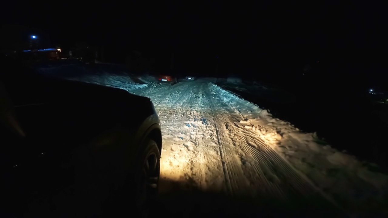 一辆大灯的汽车在夜晚滑滑的雪山路上行驶视频素材