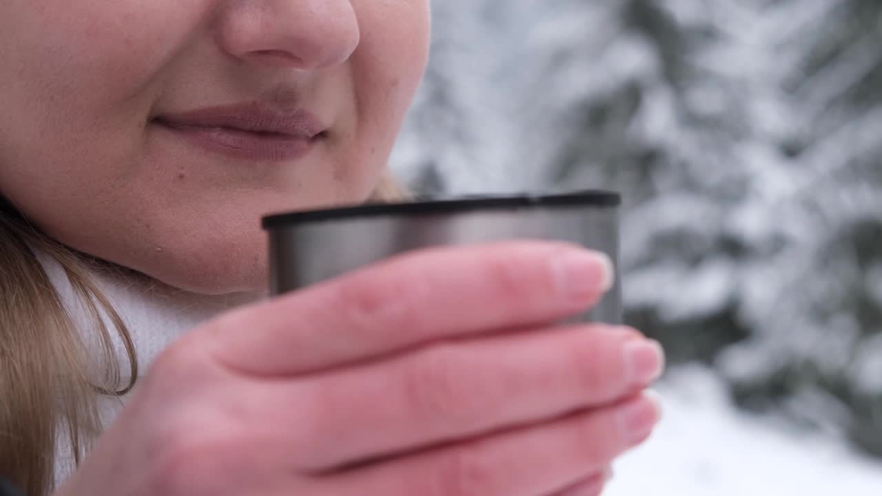 特写迷人的年轻女子喝热咖啡或茶从保温瓶在冬季雪林。视频素材