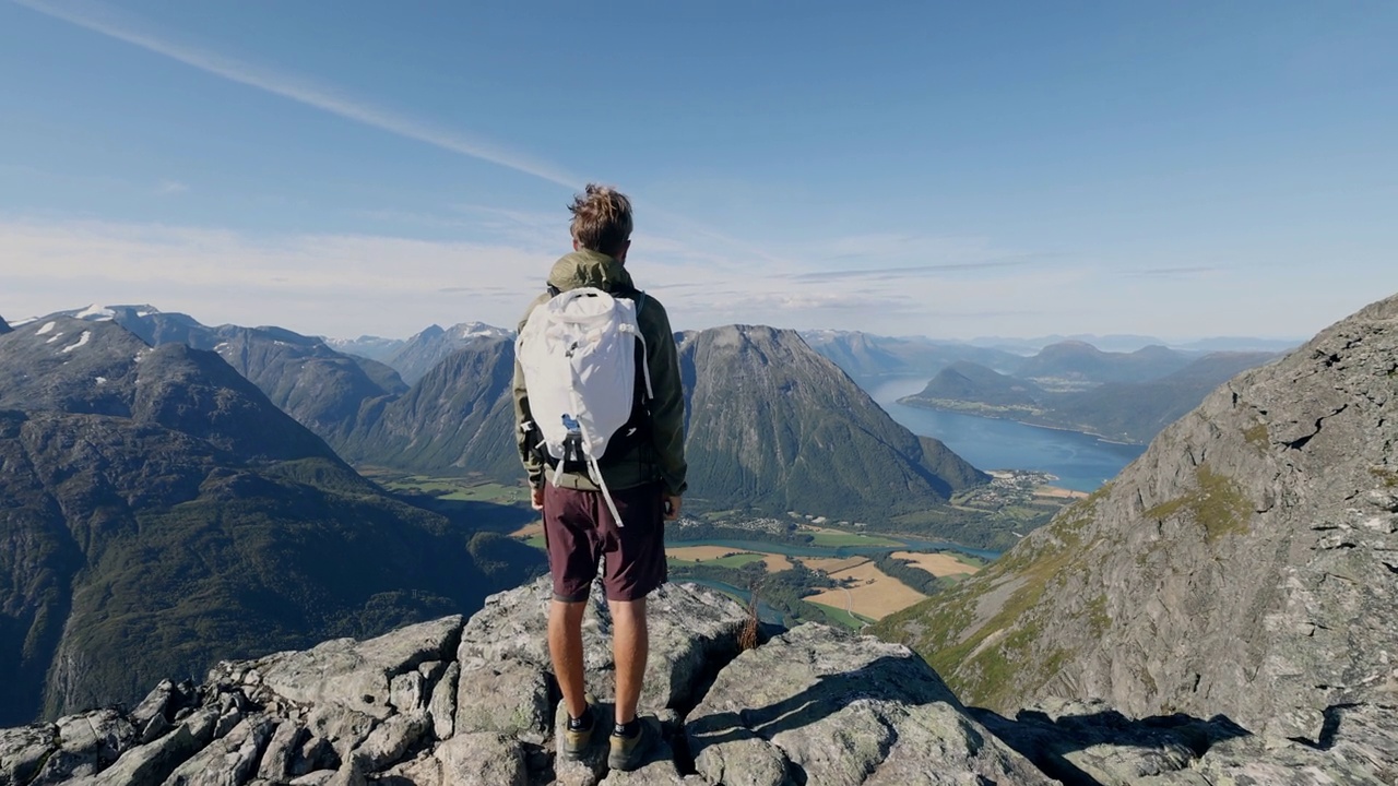 挪威徒步旅行的男子在山顶张开双臂。壮观的河流和峡湾景色视频素材