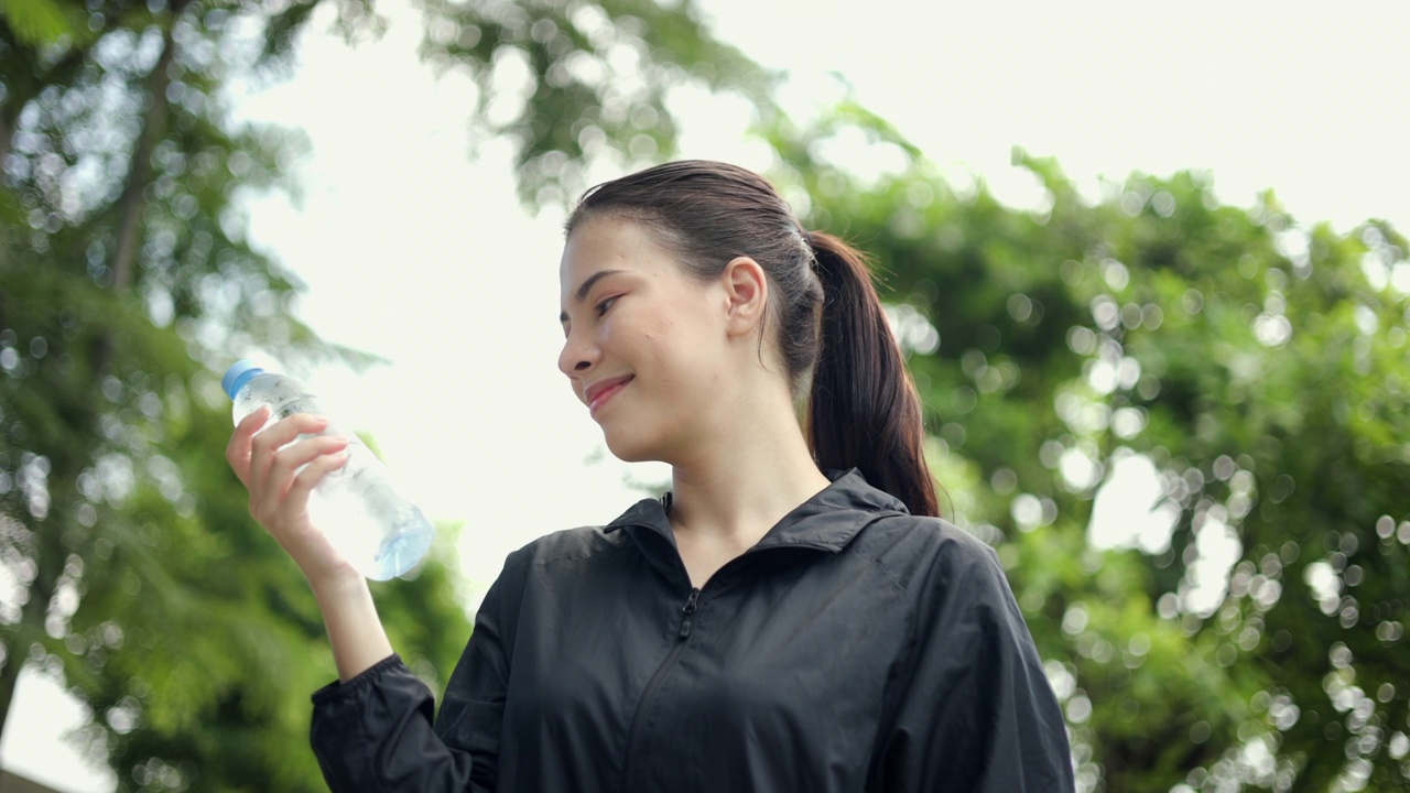 画像快乐苗条的女人在晨曦中锻炼后喝水。年轻漂亮的女性在户外慢跑后喝水。健康积极的生活方式理念。视频素材