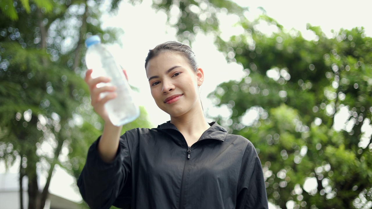 画像快乐苗条的女人在晨曦中锻炼后喝水。年轻漂亮的女性在户外慢跑后喝水。健康积极的生活方式理念。视频素材