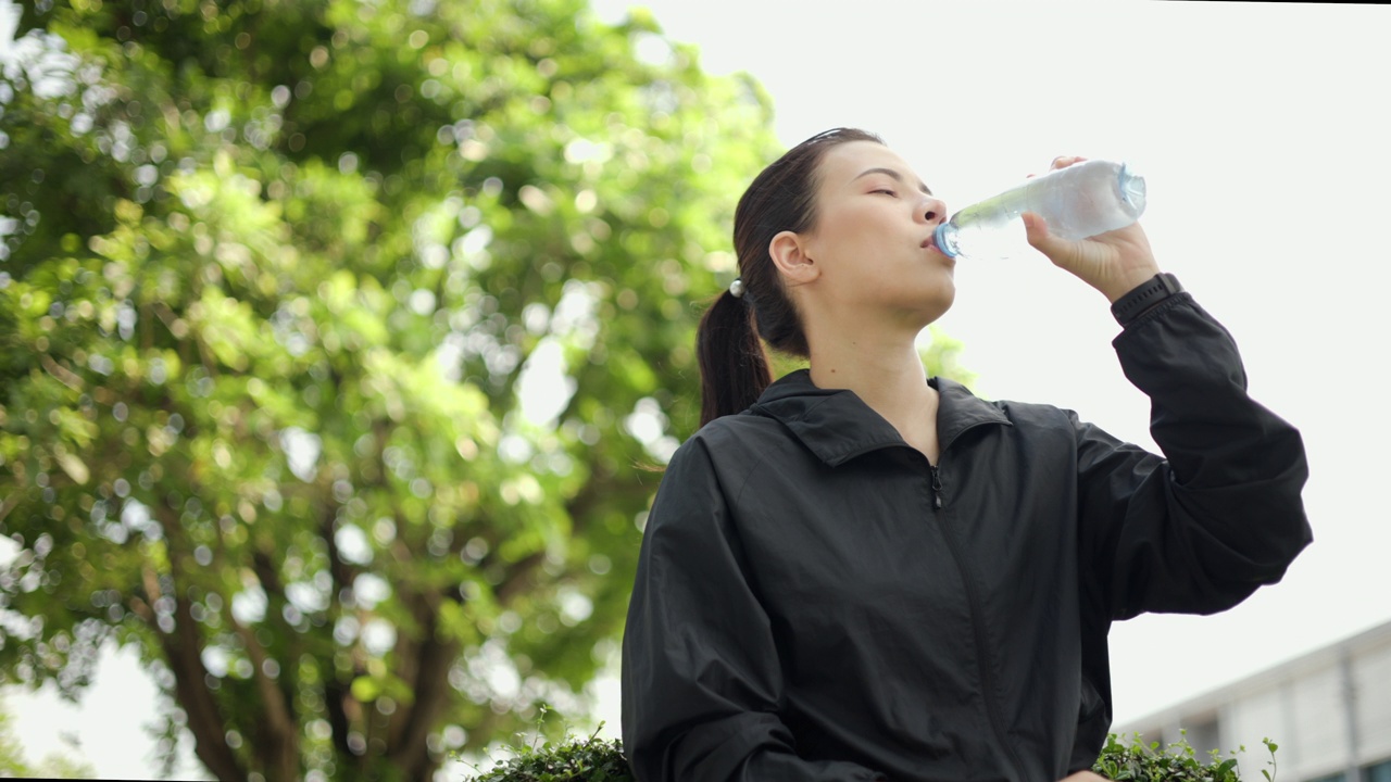 画像快乐苗条的女人在晨曦中锻炼后喝水。年轻漂亮的女性在户外慢跑后喝水。健康积极的生活方式理念。视频素材