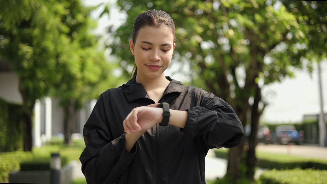 肖像年轻美丽的女人检查运动服调整智能手表在公园锻炼前。快乐运动的女性在早上锻炼和锻炼。健康积极的生活方式理念。视频素材