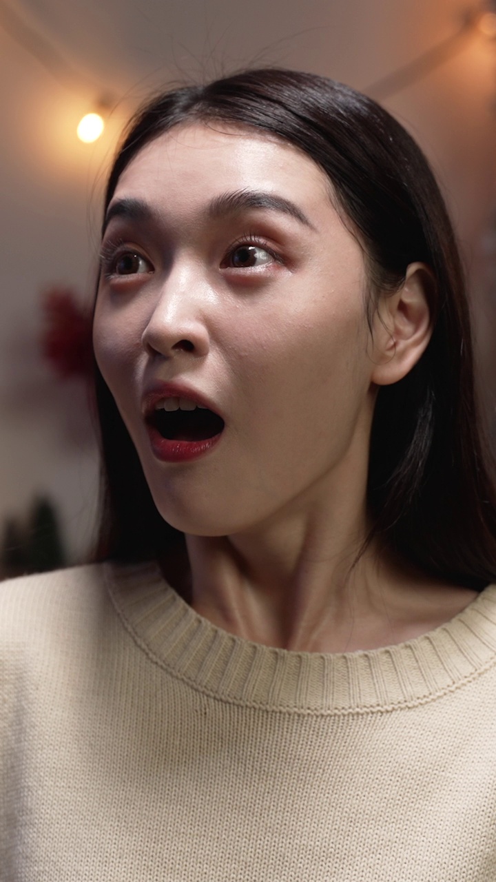 垂直屏幕:兴奋的亚洲妇女张开嘴大笑，同时手给圣诞礼物。快乐的千禧一代女性满足于情人节晚上在沙发上收到红盒子礼物视频素材