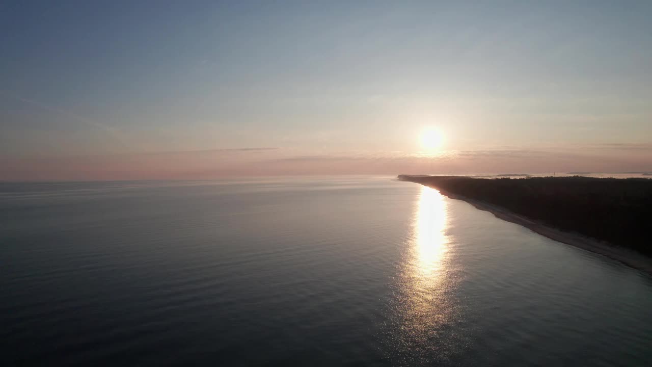 日落时空旷的海滩，无人机在水面上飞行，反射出天空的橙色。视频素材