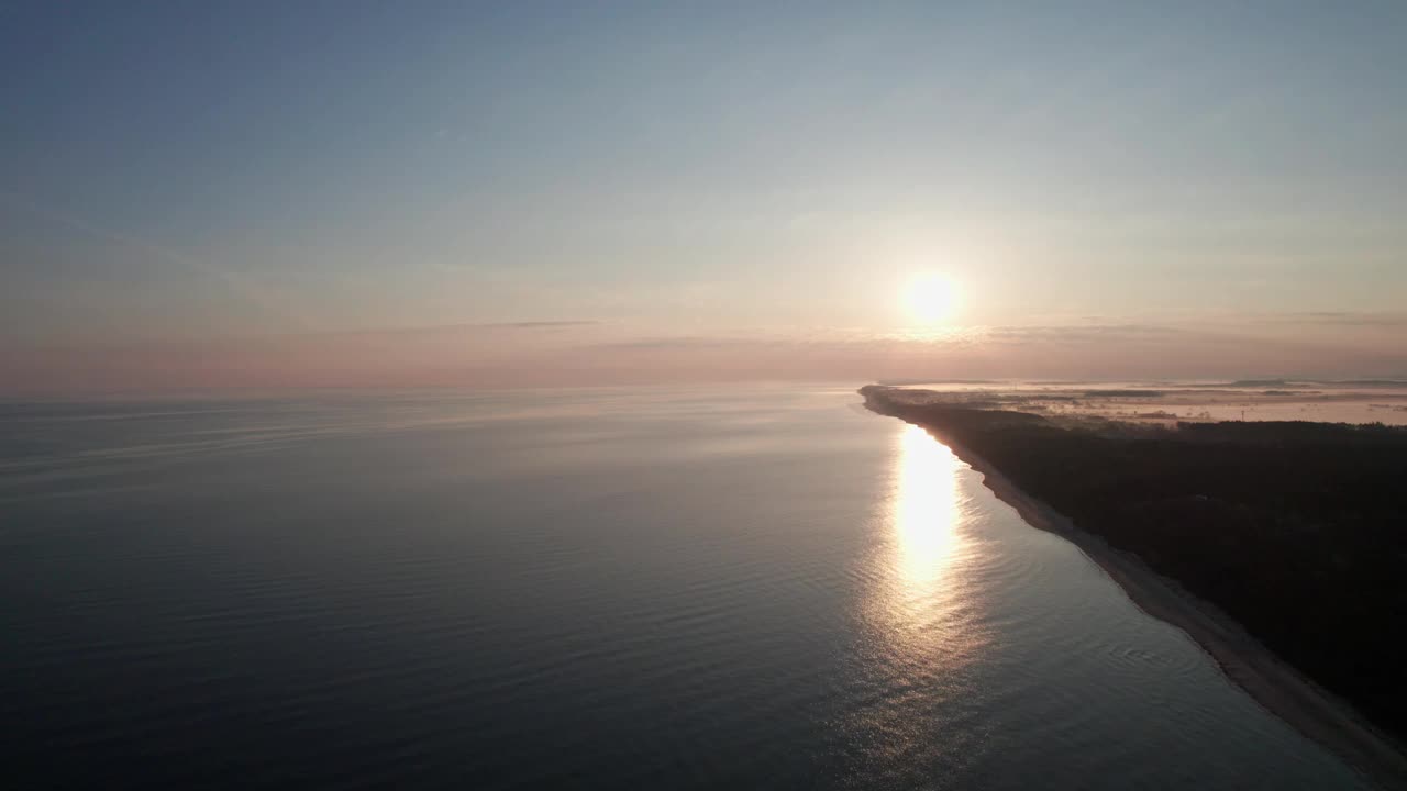 日落时空旷的海滩，无人机在水面上飞行，反射出天空的橙色。视频素材