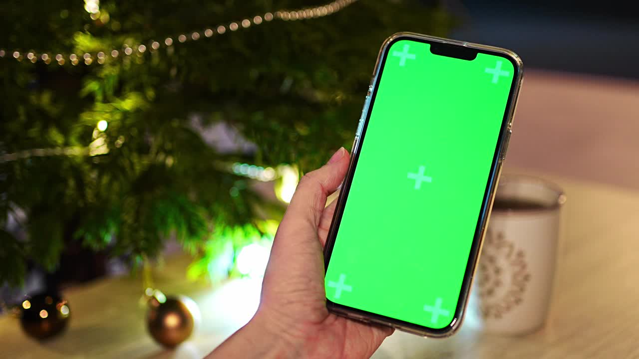 在圣诞节和新年期间，女性使用智能手机模糊图像与绿色圣诞树背景装饰彩色球。视频素材