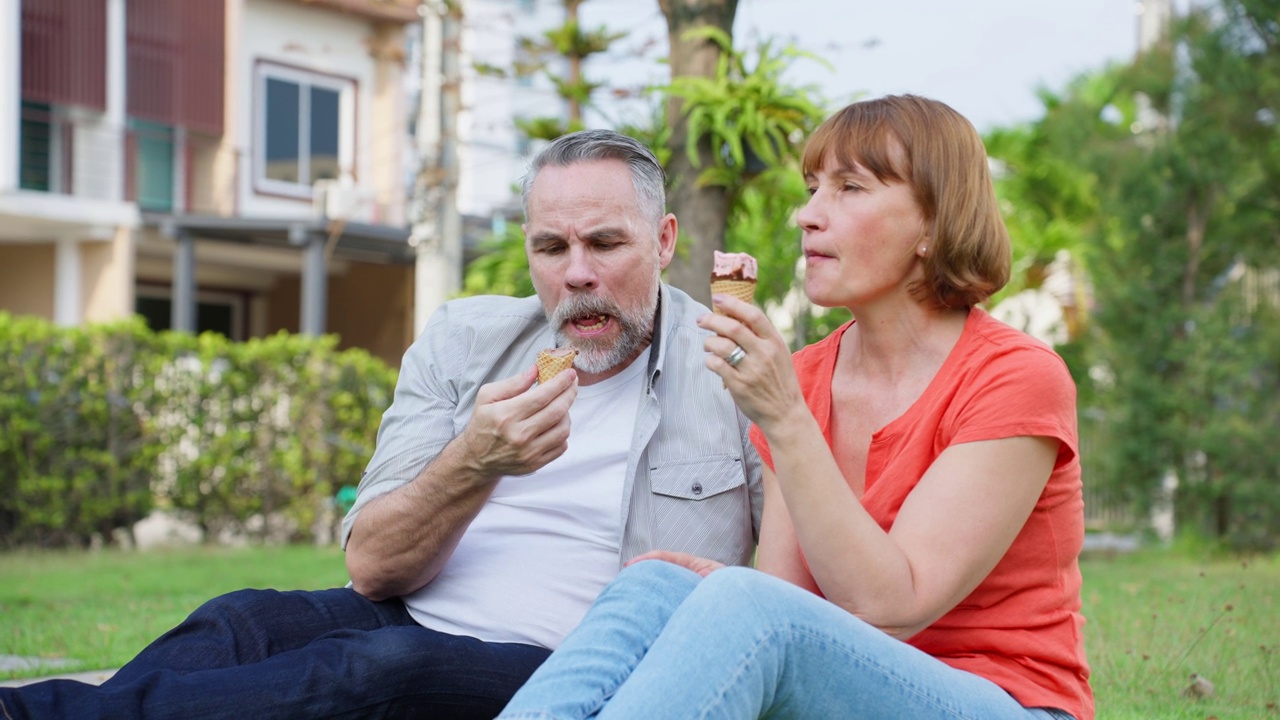 白人男子和妇女正在户外花园野餐。有吸引力的老夫妇感到快乐和放松享受退休后在公园一起吃冰淇淋的关系。视频素材