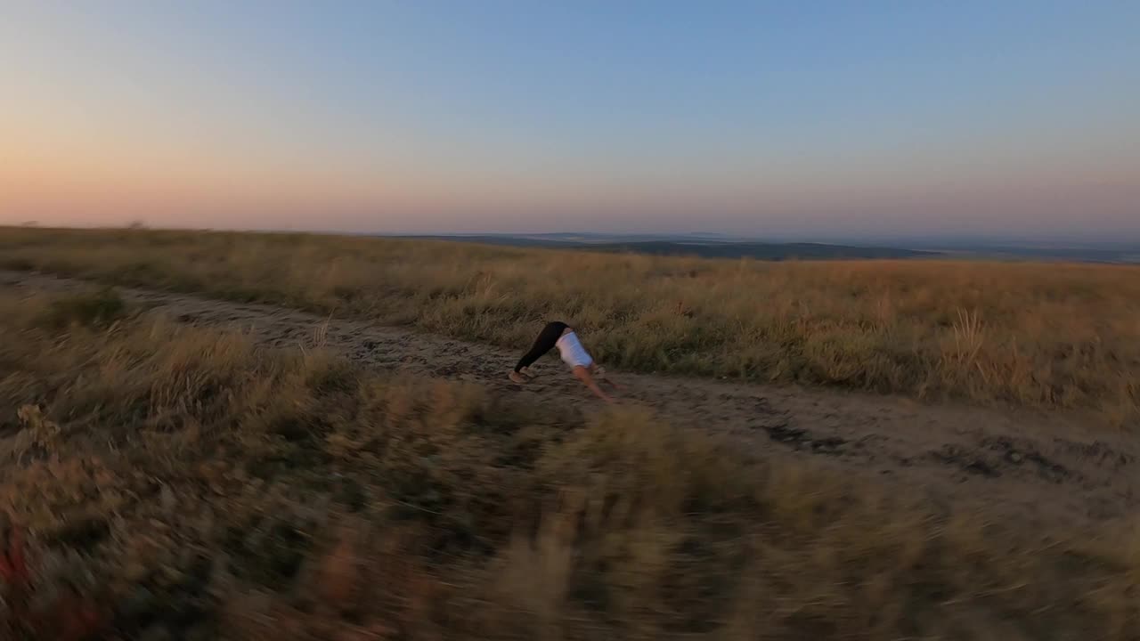 在美丽的夏日夕阳下，无人机在山顶上做瑜伽和体操的女运动员身上进行空中平移。视频素材