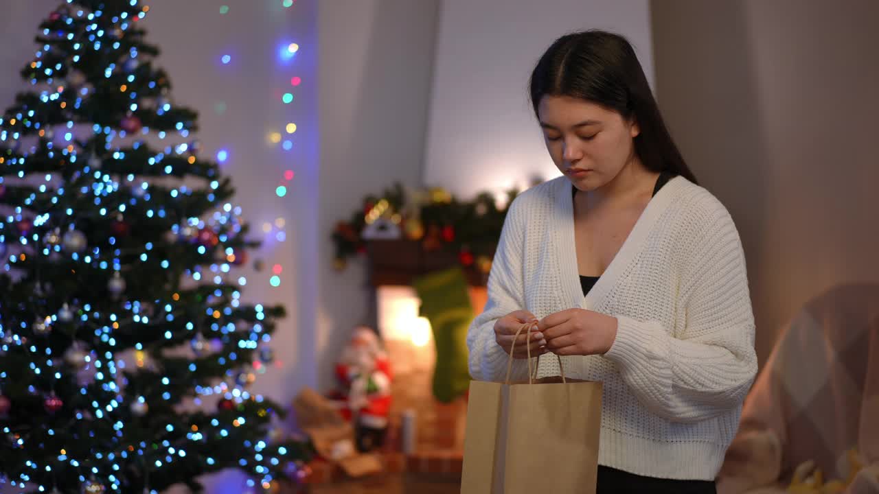 放大到不满的悲伤的亚洲妇女看着购物袋扔掉手叹息站在客厅壁炉和新年树。年轻的女士对圣诞节不满意。视频素材