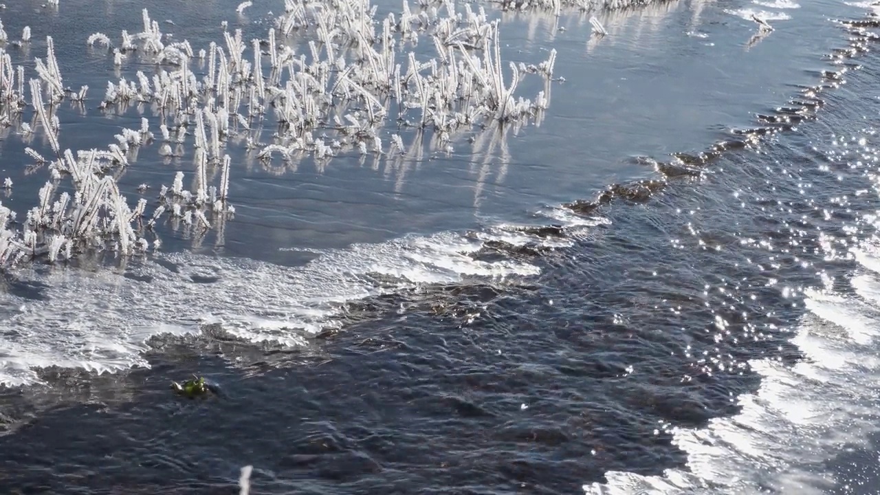 在晴朗的日子里，湍急的狭窄河流沿着结冰的河岸流淌视频素材