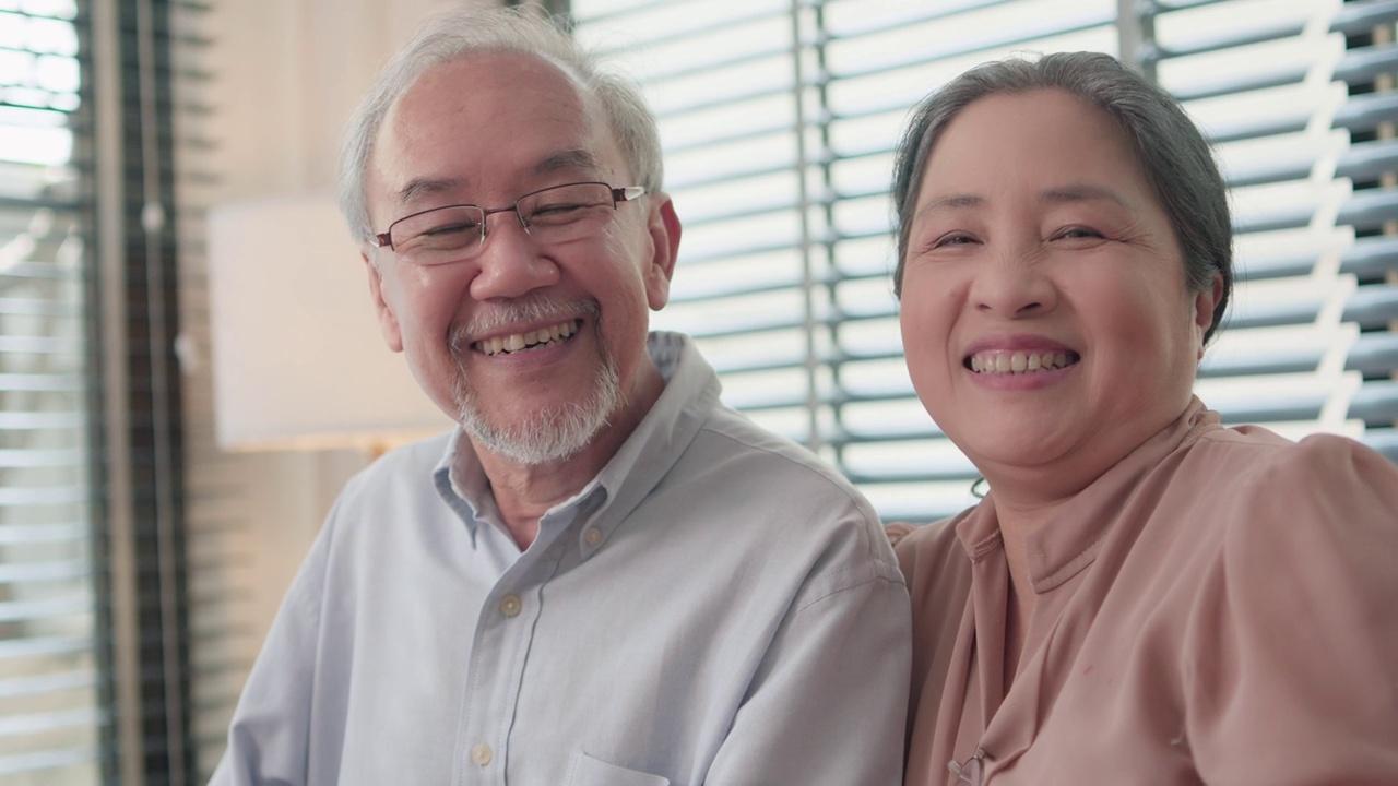 亚洲老年夫妇坐在家里客厅的沙发上一起看平板电脑。视频素材