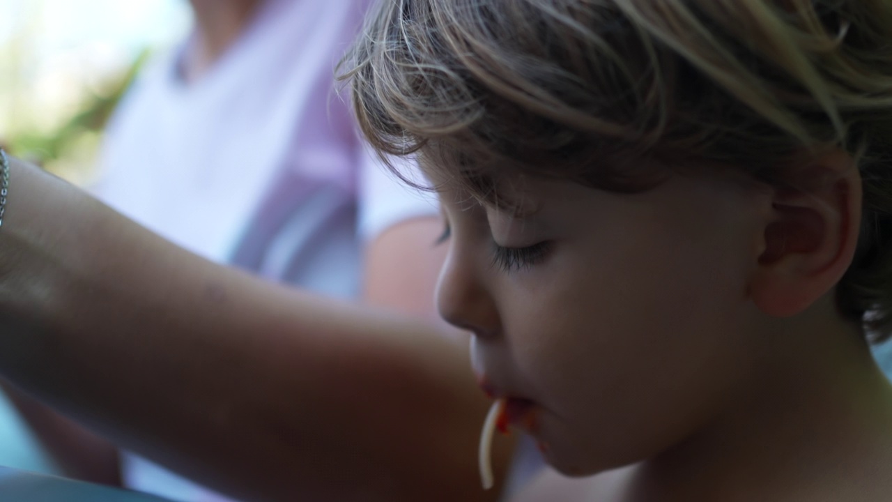 父母喂小男孩面条。孩子吃意大利面特写脸。饥饿的小孩吃碳水化合物食物视频素材