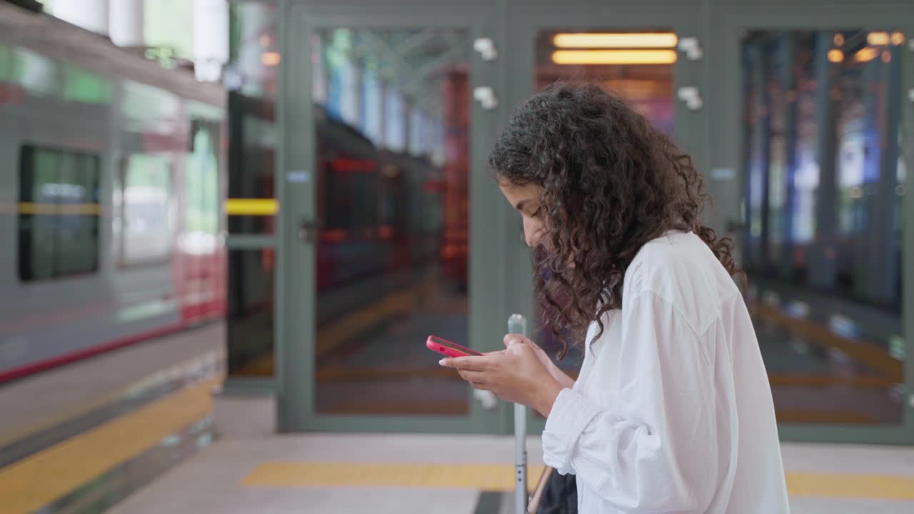 女旅客拿着手机在月台上等车视频素材