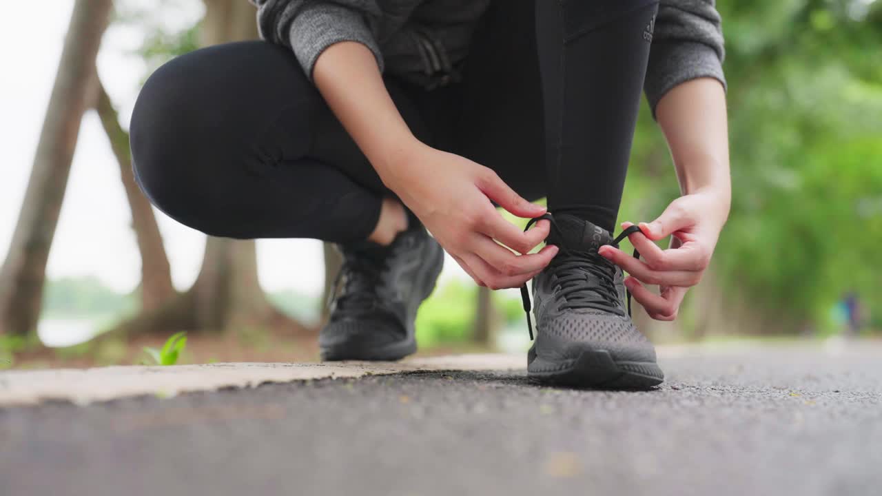 女人系鞋带的特写镜头。亚洲女性健身运动员准备在公园户外慢跑视频素材