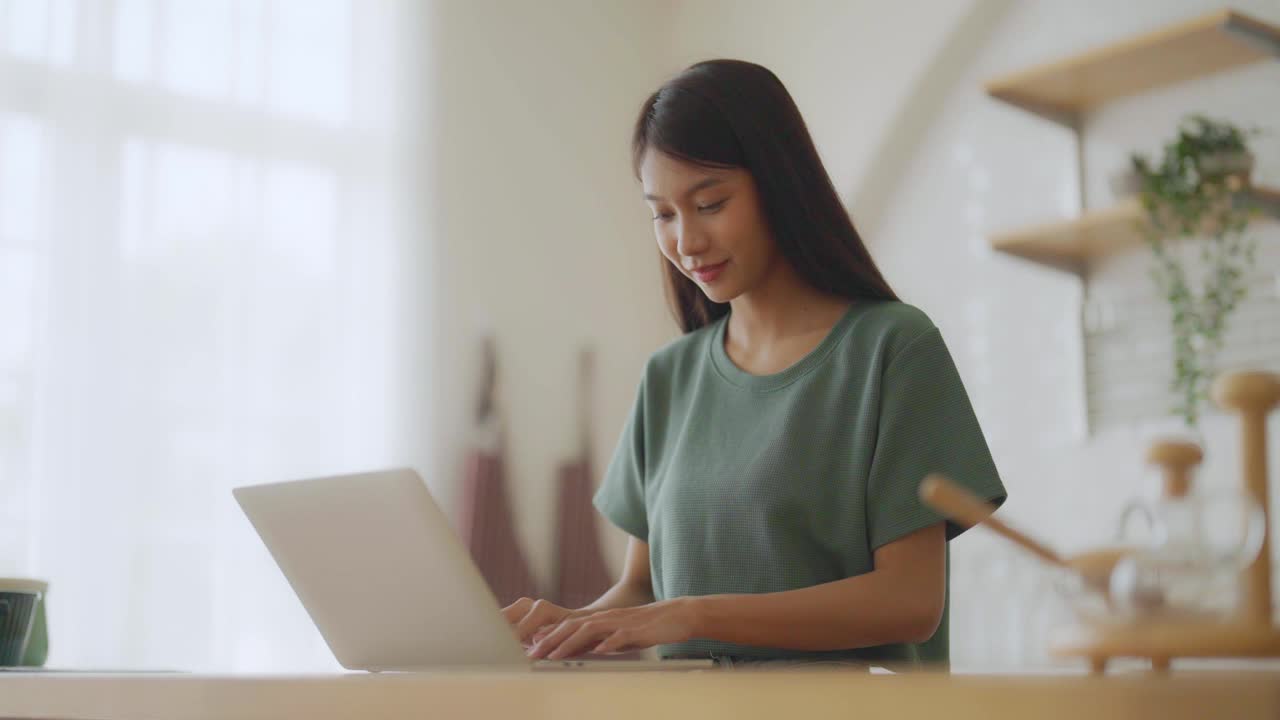 微笑的亚洲年轻女子工作在笔记本电脑在家里办公室。年轻的亚洲学生使用电脑远程学习，虚拟培训，在线学习，在家观看在线教育网络研讨会视频素材