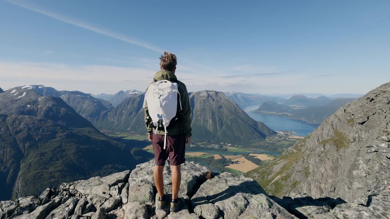 挪威徒步旅行的男子在山顶张开双臂。壮观的河流和峡湾景色视频素材