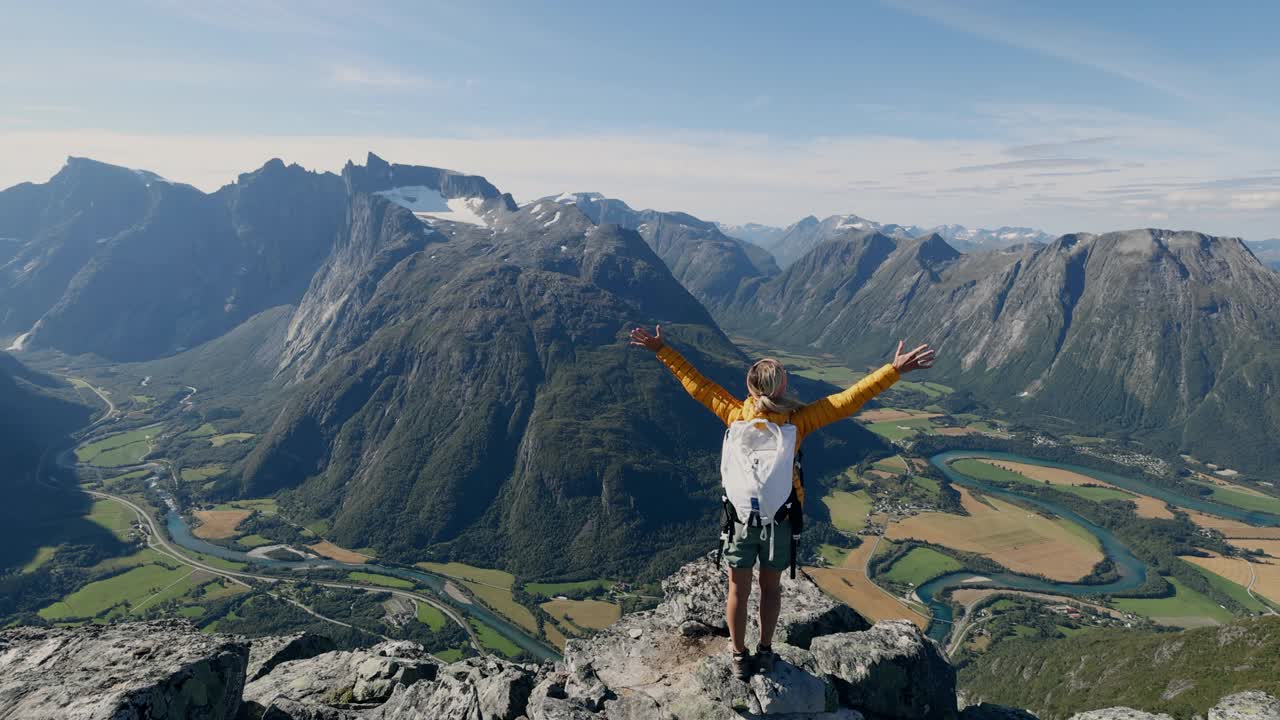 慢镜头:挪威徒步旅行的女子在山顶张开双臂。壮观的河流和峡湾景色视频素材