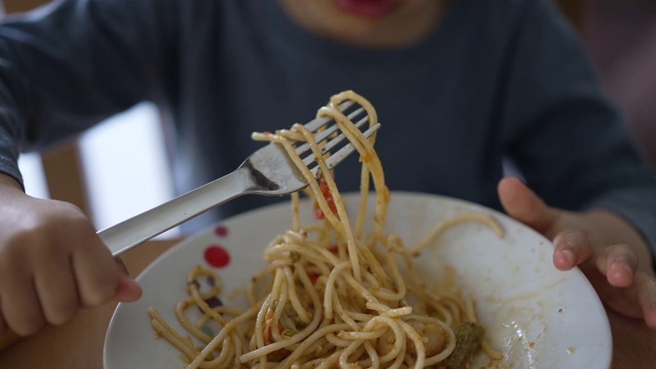 一个小男孩用叉子吃意大利面。孩子午餐吃含碳水化合物的食物。儿童营养概念视频素材