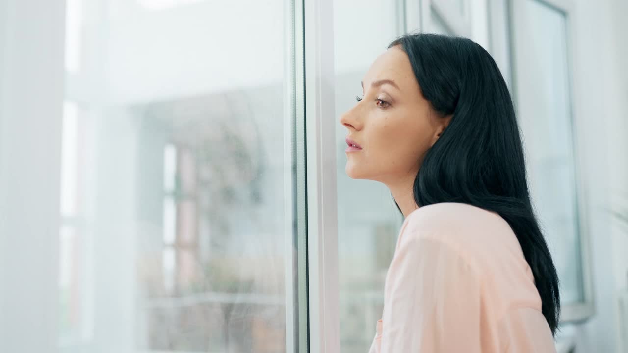 年轻女子望着窗外，思考着问题，感到孤独视频素材