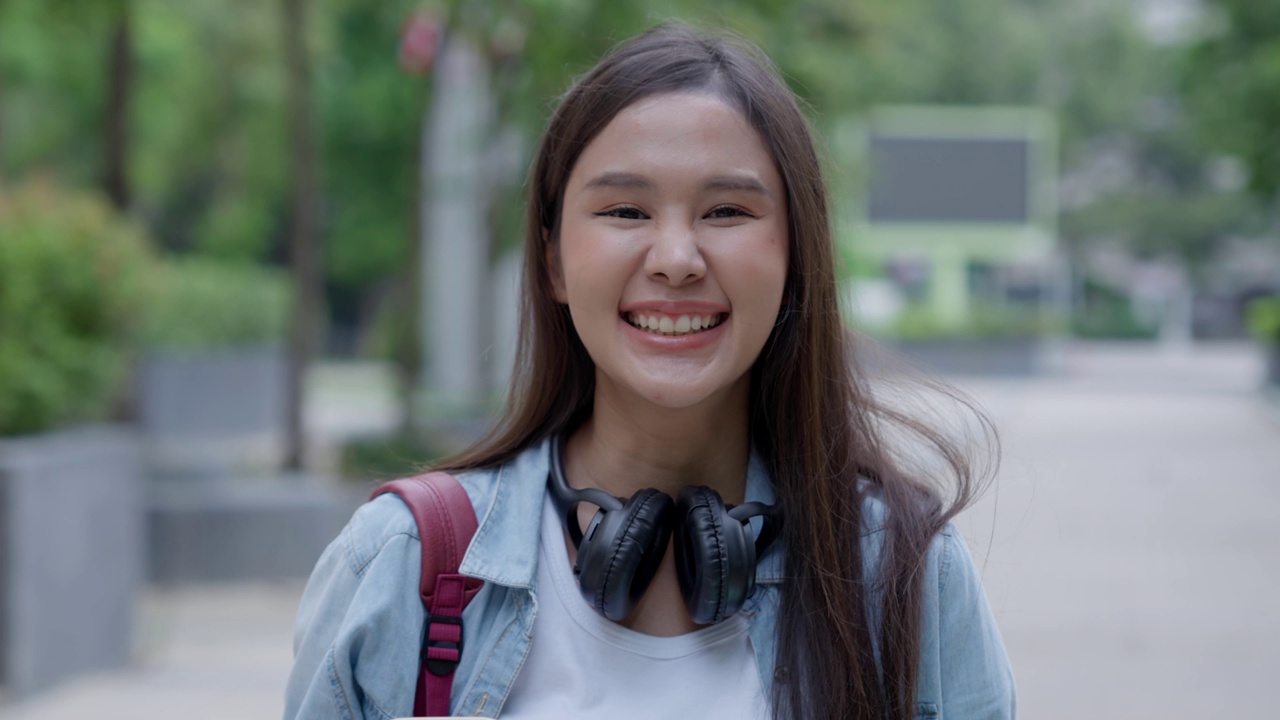 美丽的学生亚洲女人背着背包和书在户外。微笑的女孩快乐地背着很多书在大学校园。画像女上国际亚大。教育，学习，学校视频素材