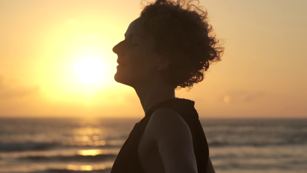 在夕阳的余晖中，一位身着夏日背心裙的女性露出了齐腰的轮廓。女人用双手拥抱自己，以此表示需要关注和关心。视频素材