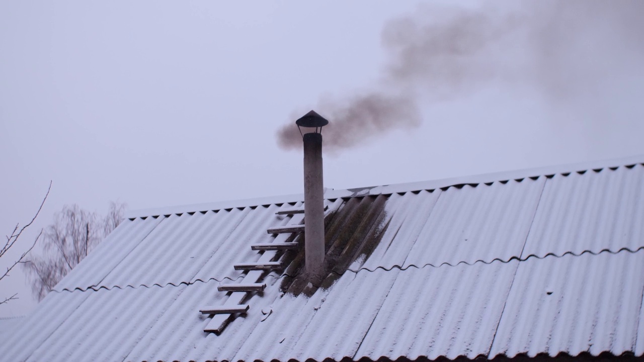 冬天，火炉的烟从澡堂屋顶的烟囱里冒出来，背景是晴朗的天空。屋顶被雪覆盖着。一缕缕烟从烟囱里冒出来。视频素材