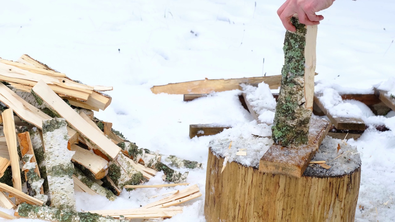 一个人在冬天的雪地里用斧头劈柴。替代供暖，木材采伐，能源危机视频素材