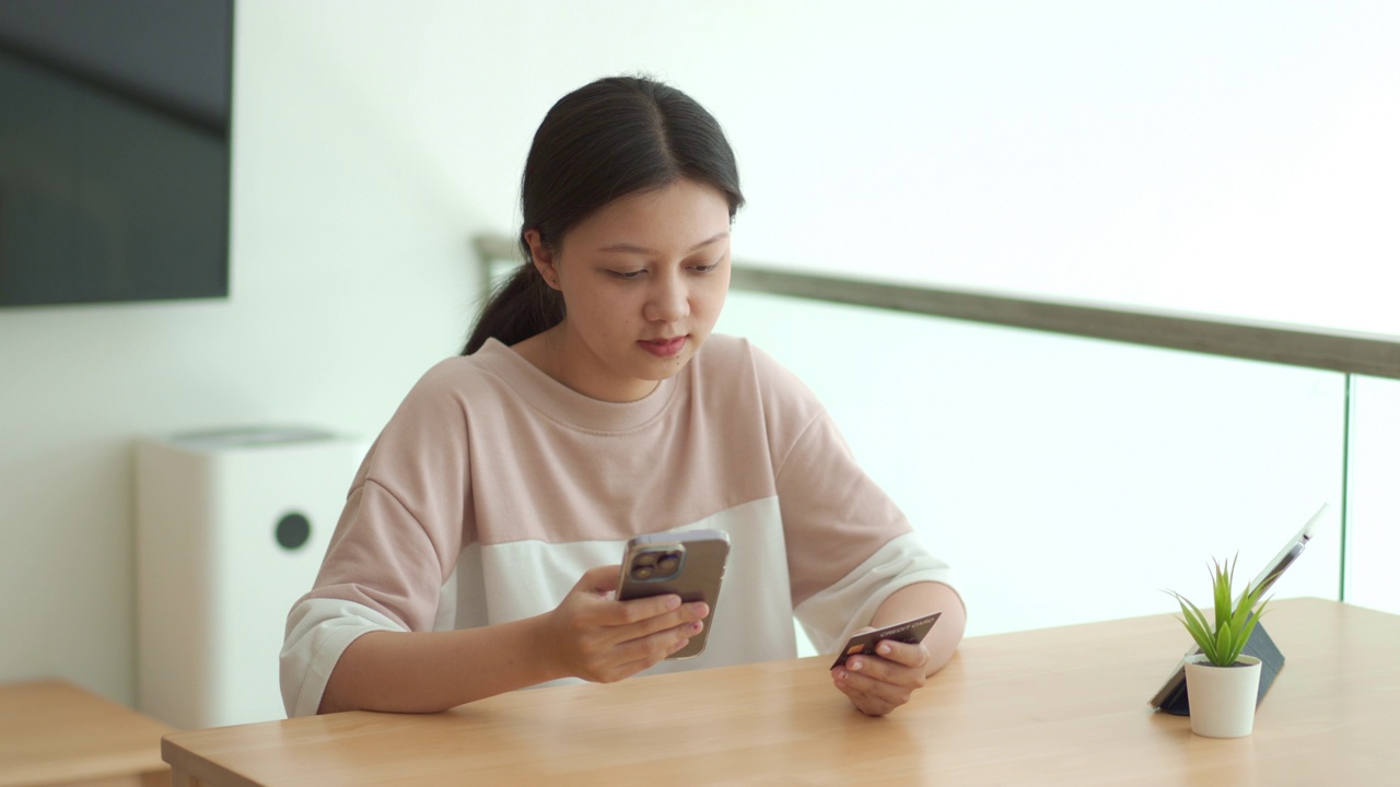 年轻成年女子的肖像，穿着休闲服，在她的智能手机上填写信用卡号码进行网上购物。视频素材