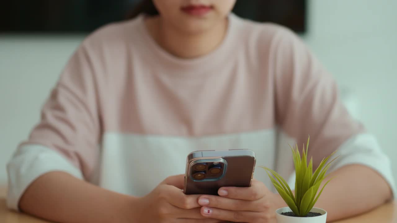 一个年轻的成年女子使用智能手机查看社交媒体，并在联合办公空间与她的朋友聊天。视频素材