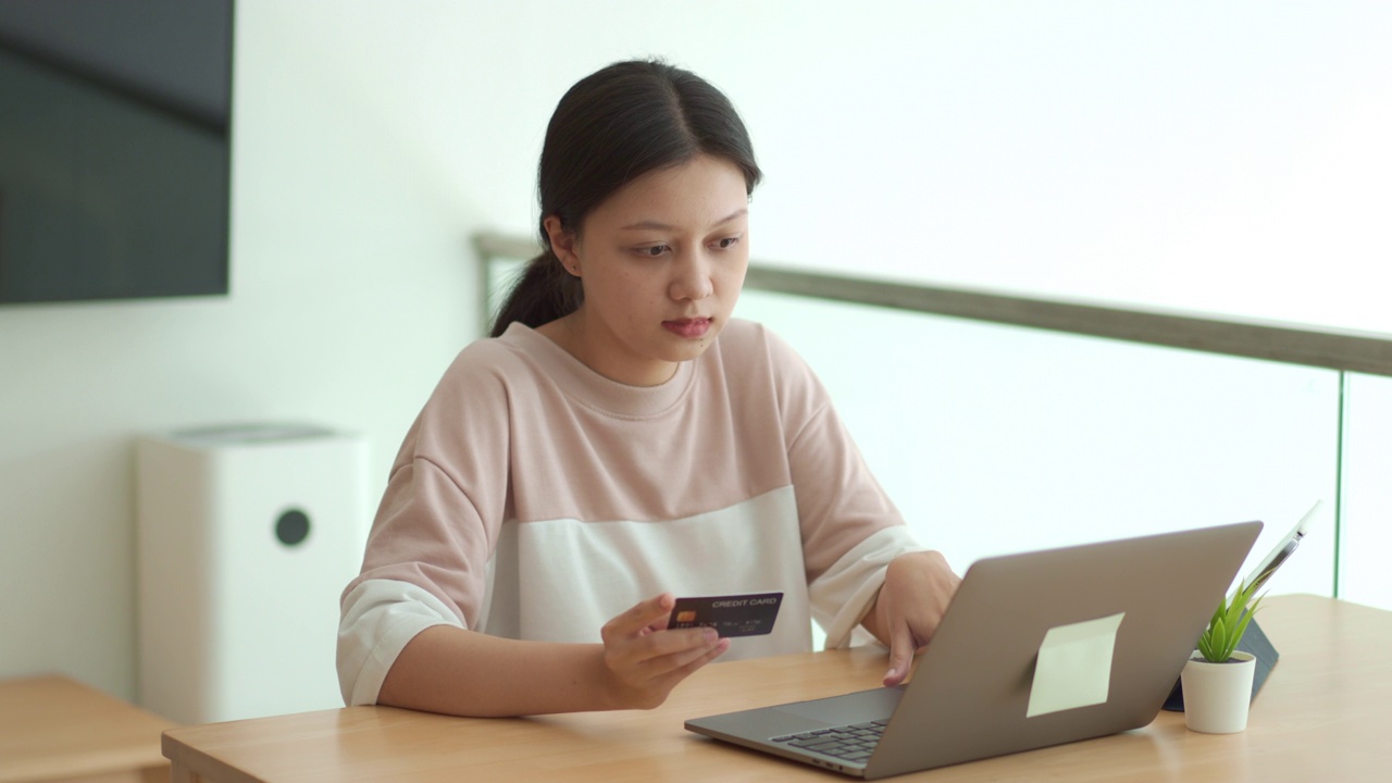 年轻女子的肖像在键盘上输入数字在她的信用卡网上购物。视频素材