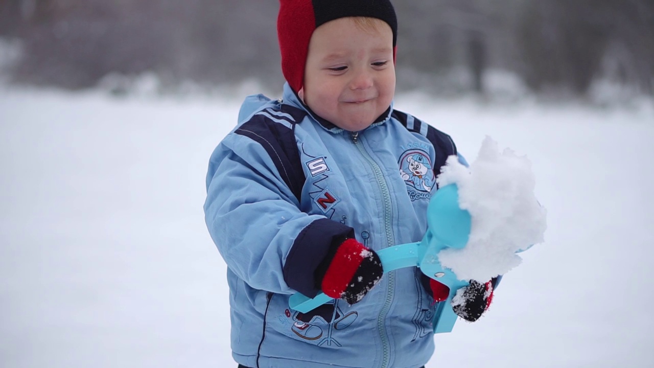 小男孩用雪球玩具把雪堆成雪球。冬天孩子们的游戏在新鲜的空气里。视频下载