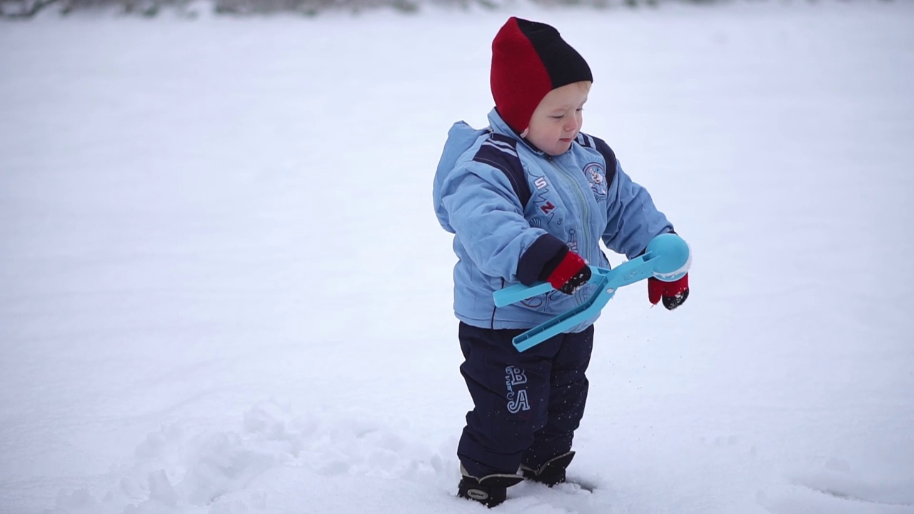 小男孩用雪球玩具把雪堆成雪球。冬天孩子们的游戏在新鲜的空气里视频下载