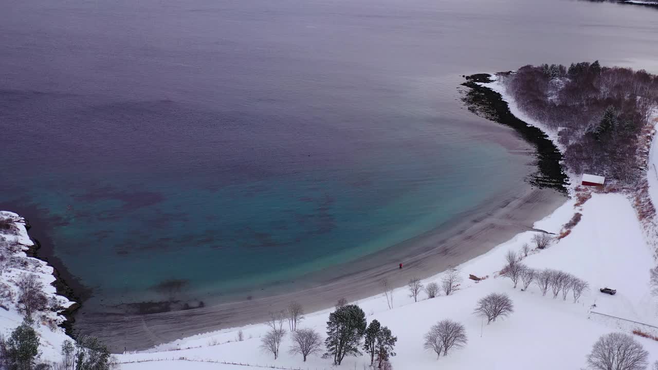 航拍的4k视频中，一名女子和一名男子在挪威的雪上走在风景秀丽的turqouse海滩上，还能看到山景视频素材