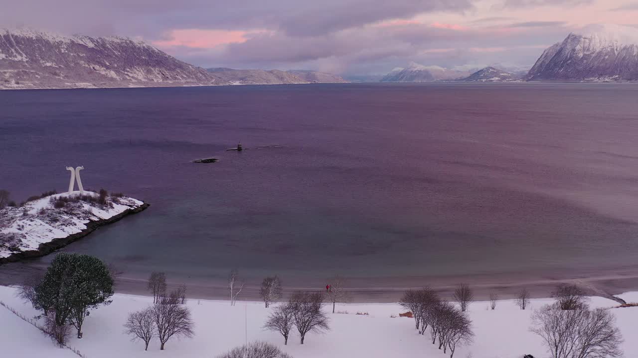 航拍的4k视频中，一名女子和一名男子在挪威的雪上走在风景秀丽的turqouse海滩上，还能看到山景视频素材