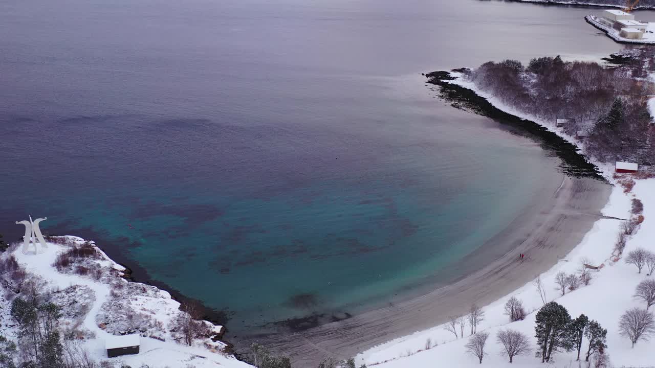 航拍的4k视频中，一名女子和一名男子在挪威的雪上走在风景秀丽的turqouse海滩上，还能看到山景视频素材