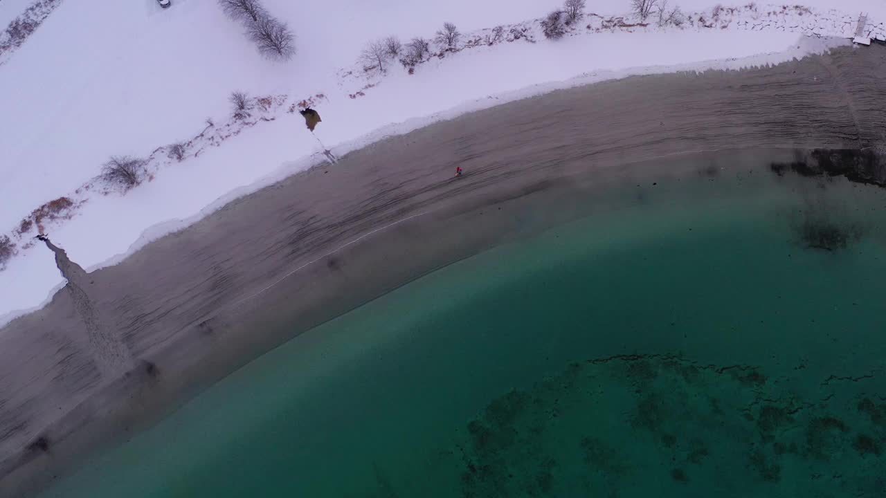 航拍的4k视频中，一名女子和一名男子在挪威的雪上走在风景秀丽的turqouse海滩上，还能看到山景视频素材