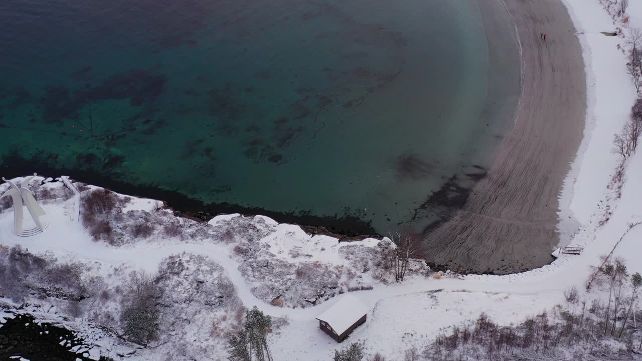 航拍的4k视频中，一名女子和一名男子在挪威的雪上走在风景秀丽的turqouse海滩上，还能看到山景视频素材