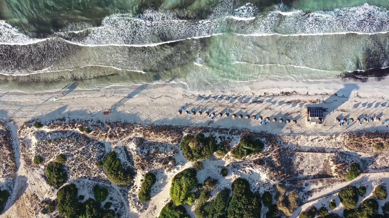 白色沙滩的空中特写，海浪到达海岸，人们在日出时散步视频素材