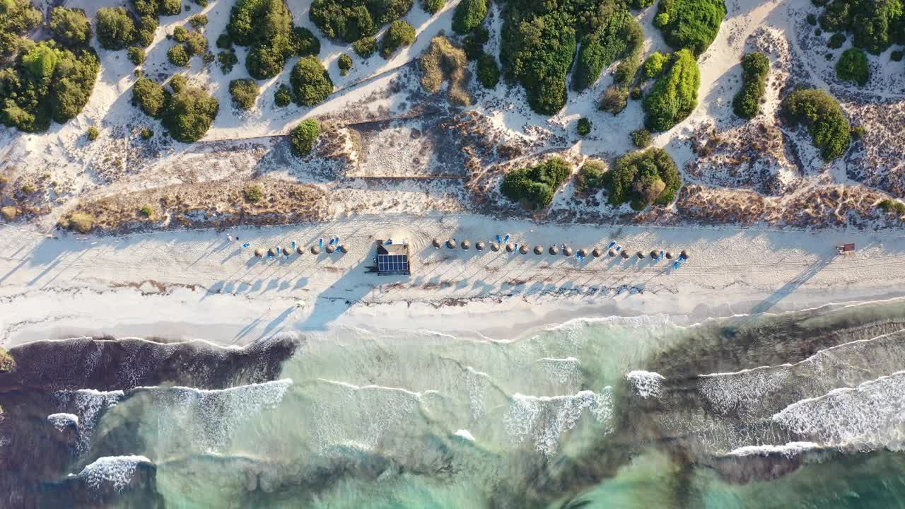 白色沙滩的空中特写，海浪到达海岸，人们在日出时散步视频下载