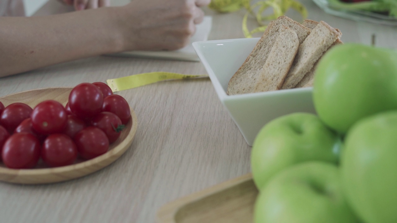 运动VDO。女人写笔记本封面上的“节食”是用来控制饮食和减肥的。妇女们写下每种食物的食物和能量的细节，以确定她们吃了多少。视频素材