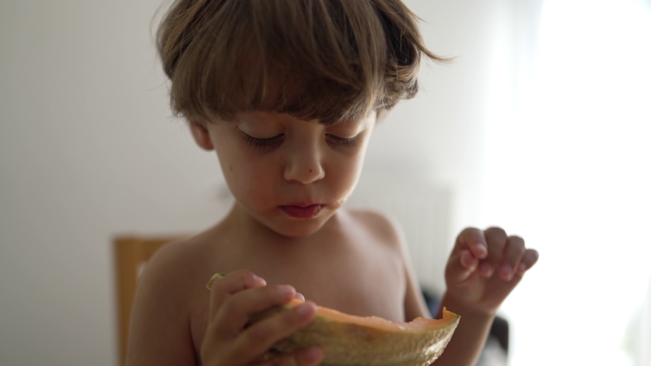 一个小男孩吃黄色瓜果的肖像。小孩在室内吃水果点心视频素材