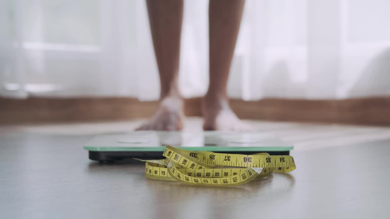 女人用皮尺踩在称上。一名女子在完成节食计划和课程后称体重。饮食概念和减肥。视频素材