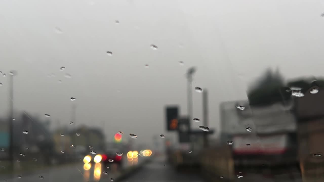 恶劣的阴雨天气，雨点滑落在挡风玻璃上，背景中车辆灯光模糊视频素材