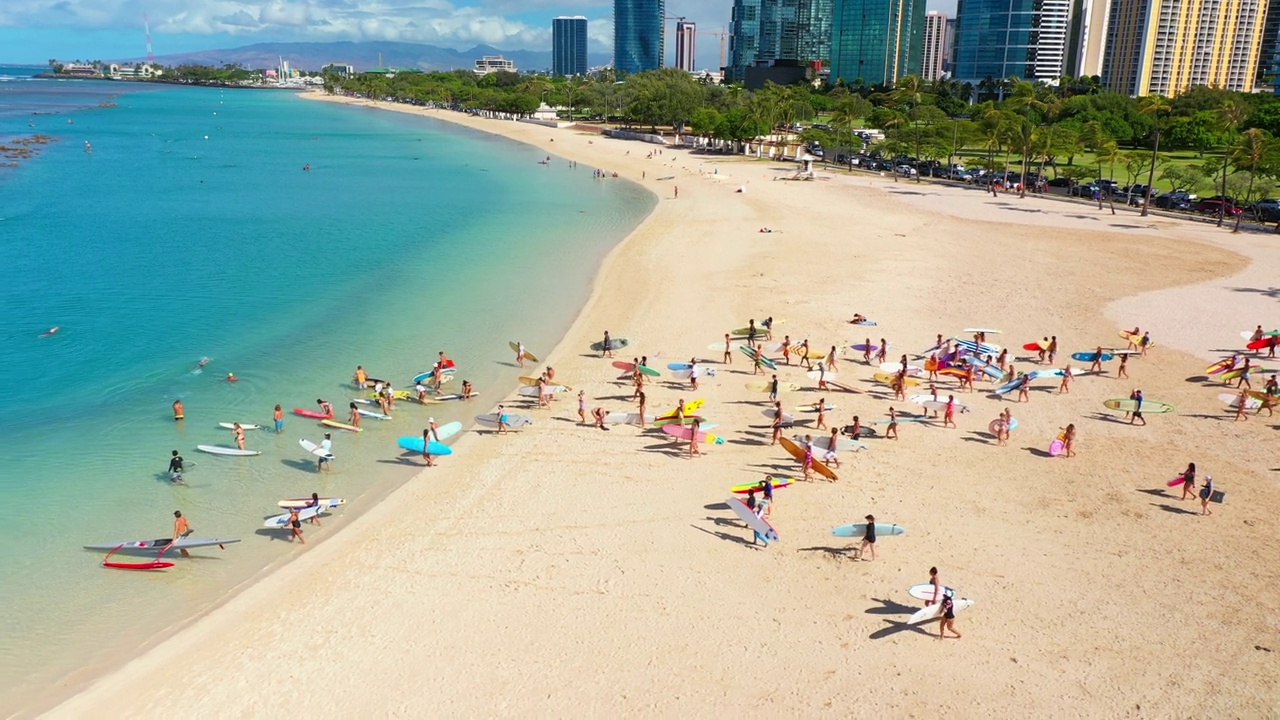 阳光明媚的一天，冲浪者带着冲浪板走向大海的空中平移镜头——夏威夷瓦胡岛视频素材