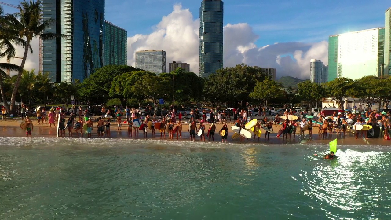 摇摆镜头的男性和女性冲浪者与冲浪板在海岸线在城市对多云的天空-瓦胡岛，夏威夷视频素材